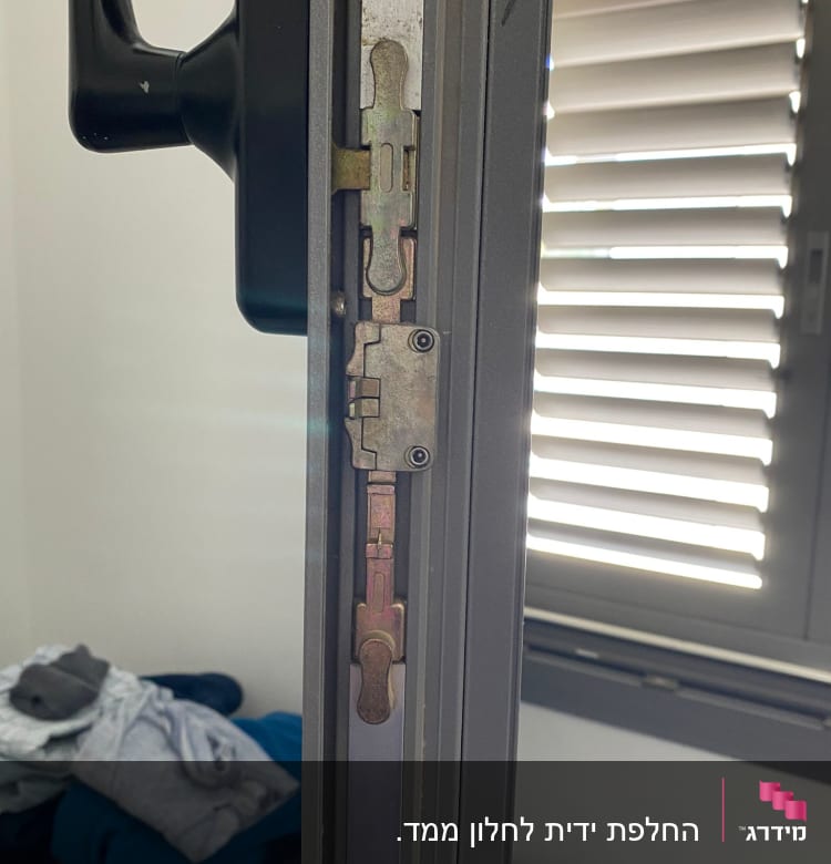 חלון עם תריסים סגורים חלקית ומנגנון נעילה גלוי